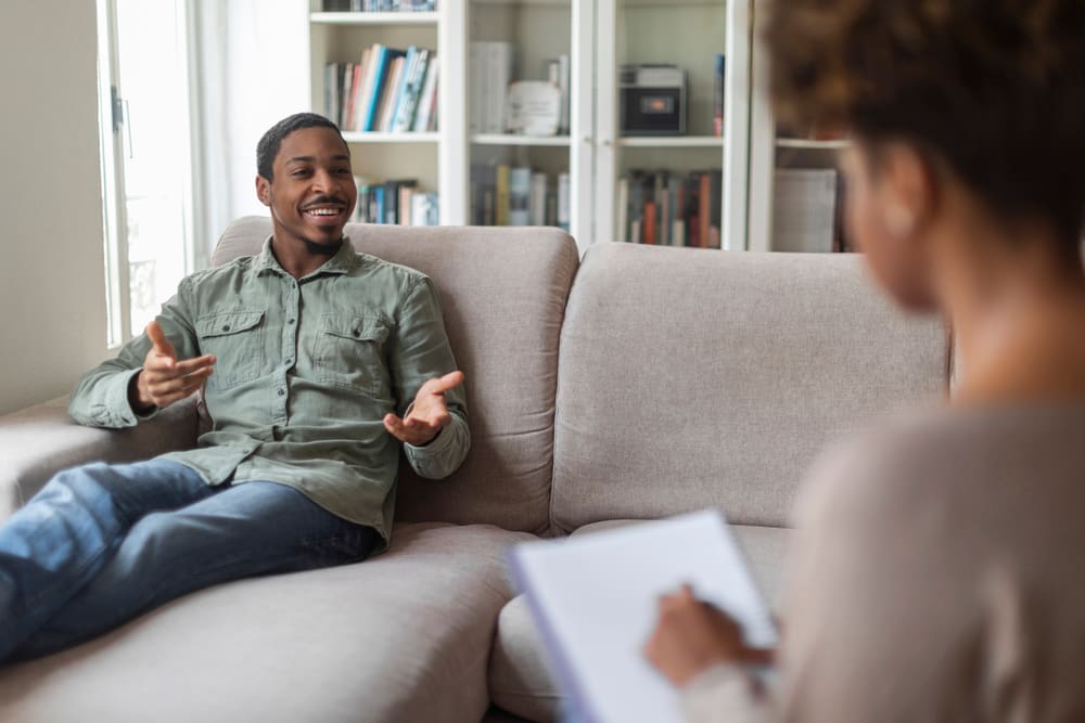 Inspired thrilled young man in casual reclining on couch at counselor office, sharing feelings, thoughts with therapist