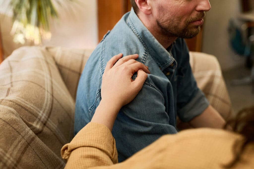 Concerned person placing a hand on a man’s shoulder while checking on his well-being after drinking.