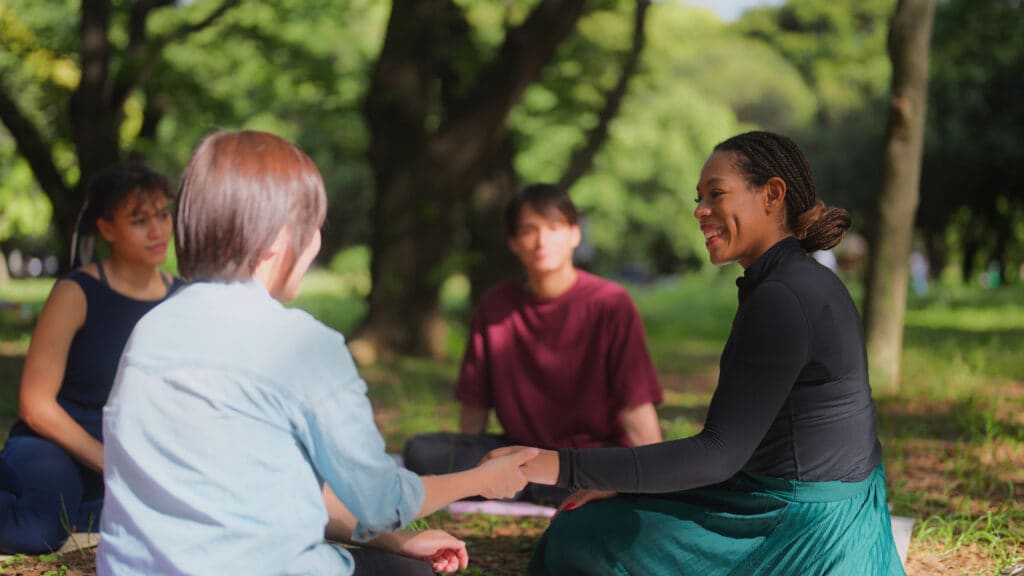 Diverse adults participating in an outdoor recovery support circle focused on connection and shared healing.