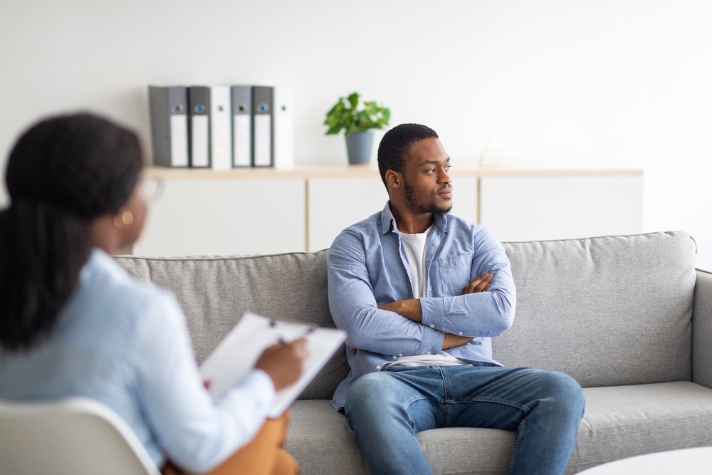 psychologist working with emotionally detached black male patient at clinic, trying to help him with addiction