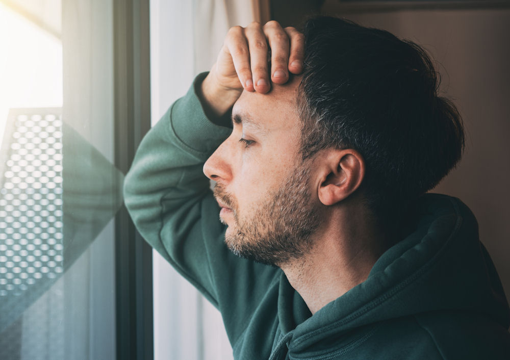 Man looking out window, stressed by dangers of mixing opioids with benzos