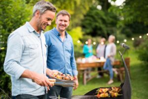 men prepares a barbecue for friends gathered around a table in the garden