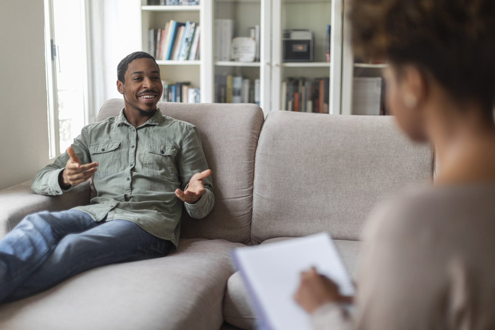 Inspired thrilled young man in casual reclining on couch at counselor office, sharing feelings, thoughts with therapist