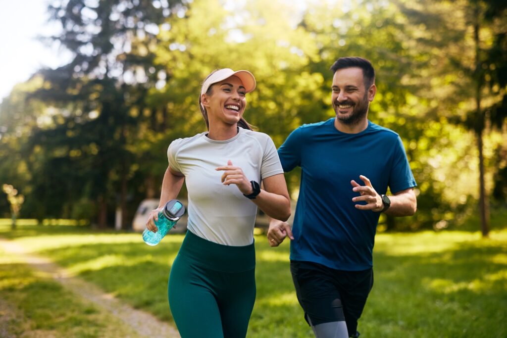 Cheerful athletic couple jogging through park.