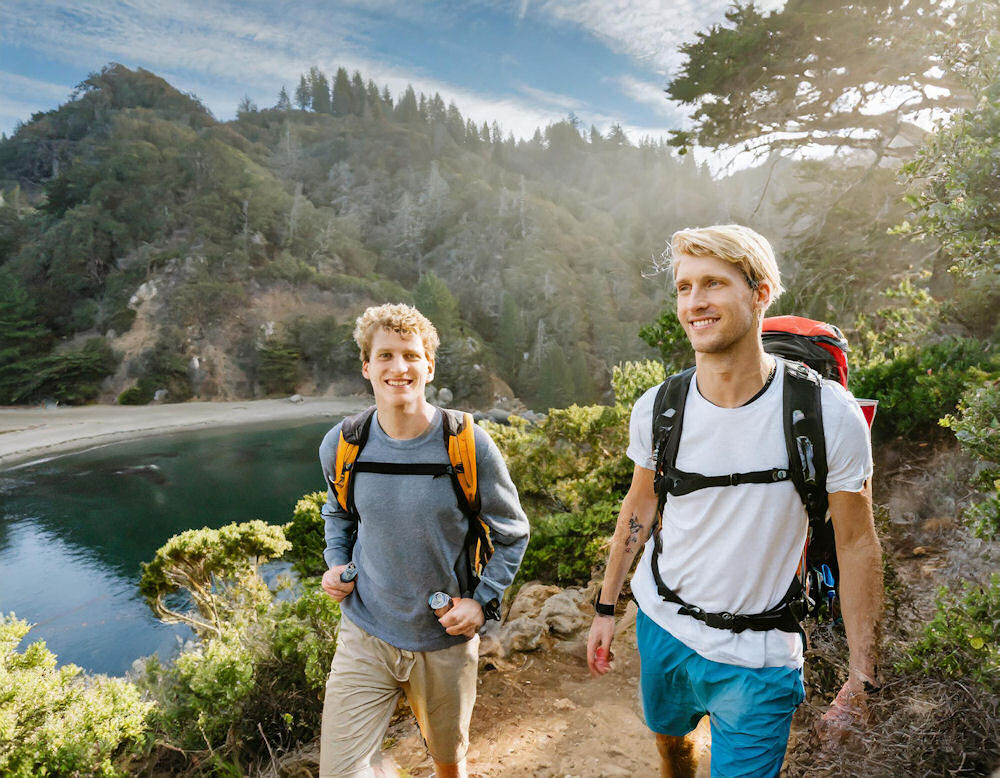 Two young men walking with hiking backpacks in outdoor adventure therapy.