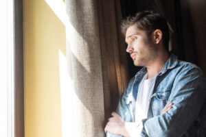  picture of a man in a looking from a window showing signs of anxiety and depression