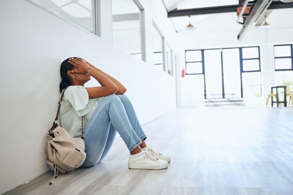 Sad, depression and anxiety student woman on floor in university campus classroom