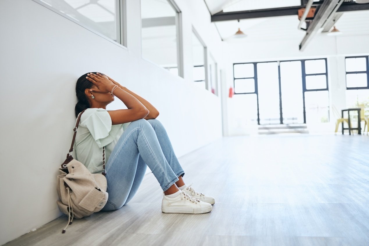 Sad, depression and anxiety student woman on floor in university campus classroom 