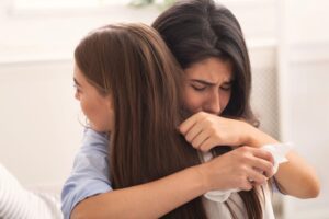 Friendship And Support. Depressed Girl Crying Hugging Her Compassionate Friend Complaining About Problems Sitting On Couch Indoor.