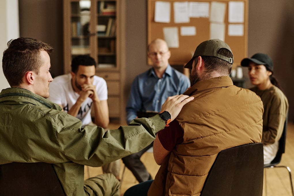 Support group tapping shoulder of upset man while comforting him