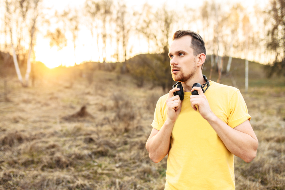 athletic guy with headphones outdoors at sunset