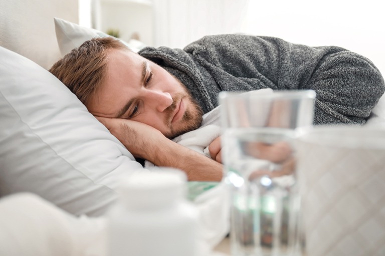 First responder in bed with depression while pills and full water glass are on a nightstand in foreground