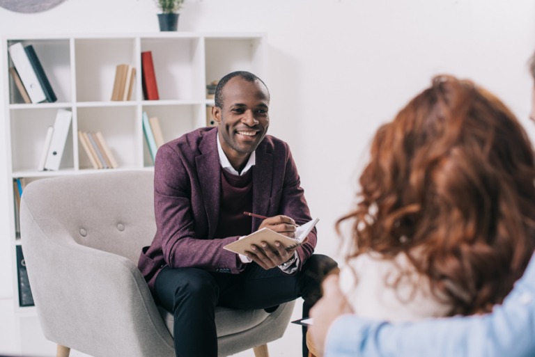 Smiling eating disorder therapist talking with young patient with long red hair