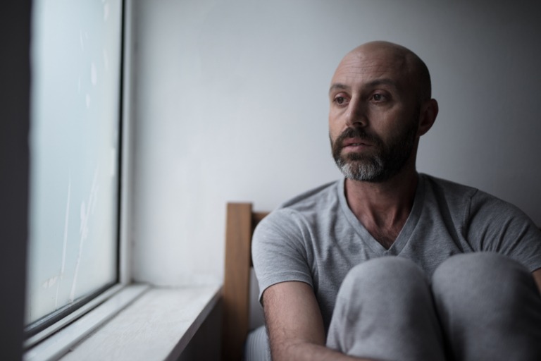 Sad man looking out the window wondering how to help a friend with a gambling addiction