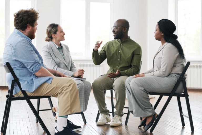 Therapist with glasses instructing about recovery from addiction in small group of older people with addiction