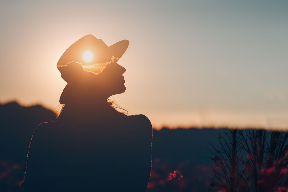 Special shadow portrait of the sun setting in front of a woman wearing a fedora