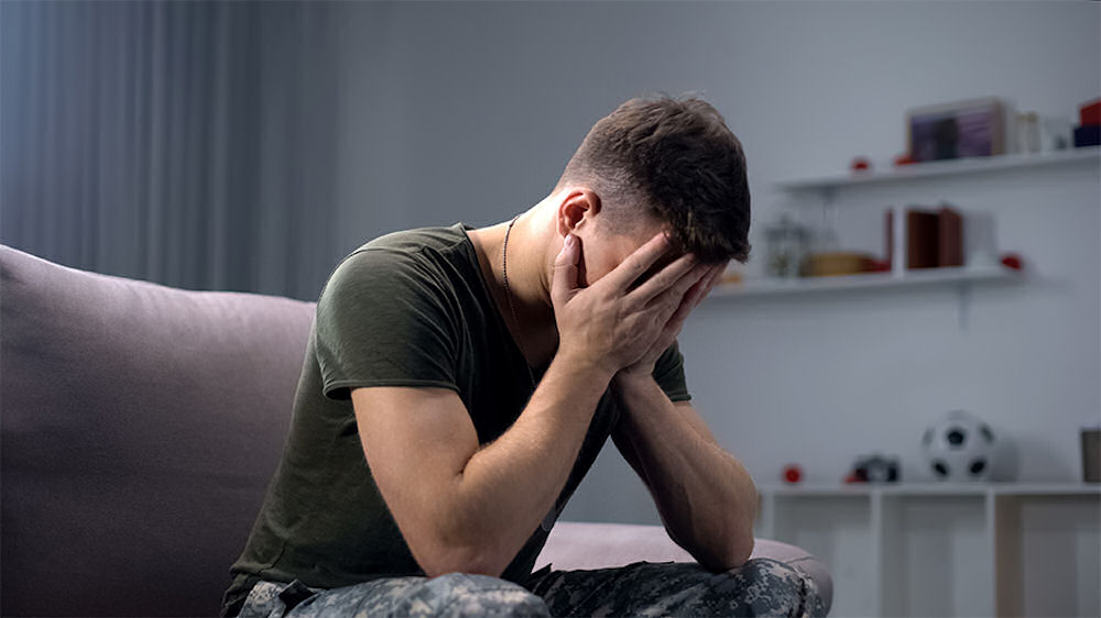 Man in fatigues covering face in hands while going through alcohol withdrawal