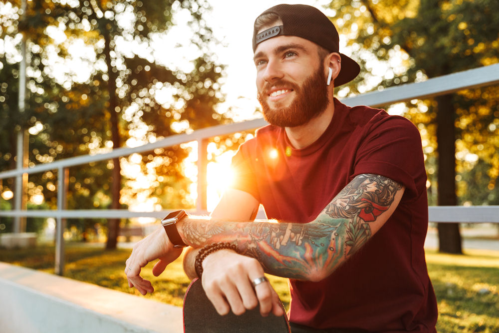 Happy young man with tattoos and ear pods listening to music in a stadium.