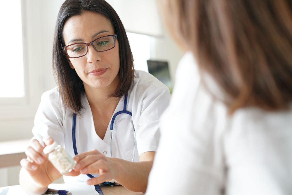 Doctor explaining prescription label on pill bottle to female patient.