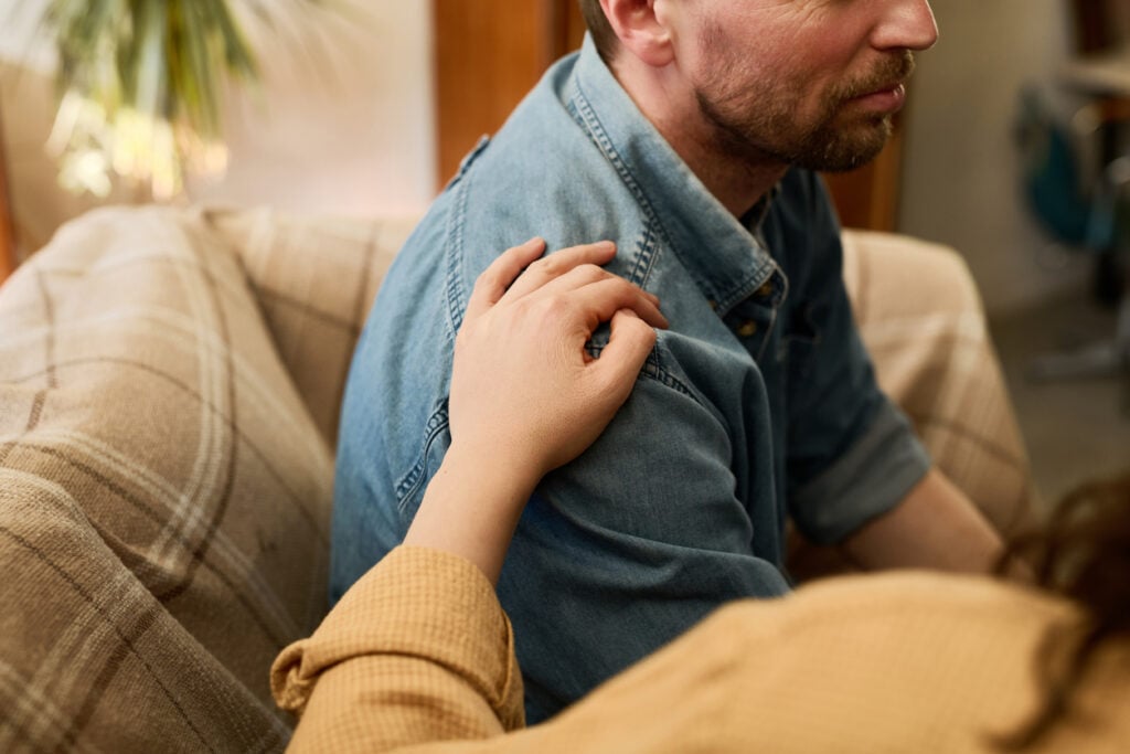 Concerned person placing a hand on a man’s shoulder while checking on his well-being after drinking.