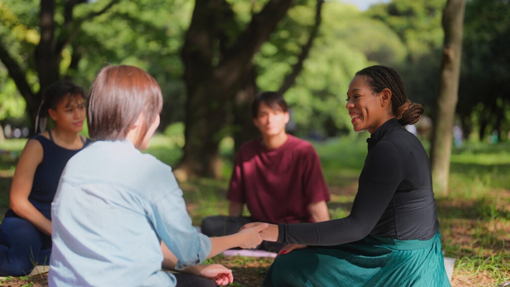 Diverse adults participating in an outdoor recovery support circle focused on connection and shared healing.